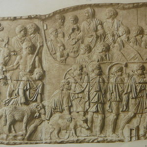 76. Trajan stands in the vestments of the Great Pontiff. His right hand holds a patera for pouring wine on the altar during the sacrifice before a new military campaign. On the left are three sacrificial animals: a pig (sus),a ram (ovis) and a bull (taurus). They are preceded by bucinator,cornicene,and tubucene. This is the scene of the beginning of the last military campaign of 106