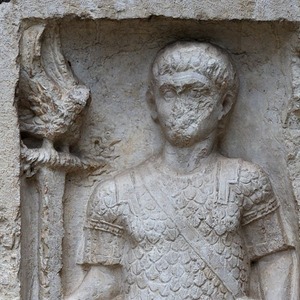 Деталь надгробного рельефа Луция Сертория Фирма, аквилифера Legio XI Claudia Pia Fidelis: фигура в чешуйчатом доспехе и аквила на древке. Верона, Museo Lapidario Maffeiano, инв. 28161; известняк, I в. н.э.